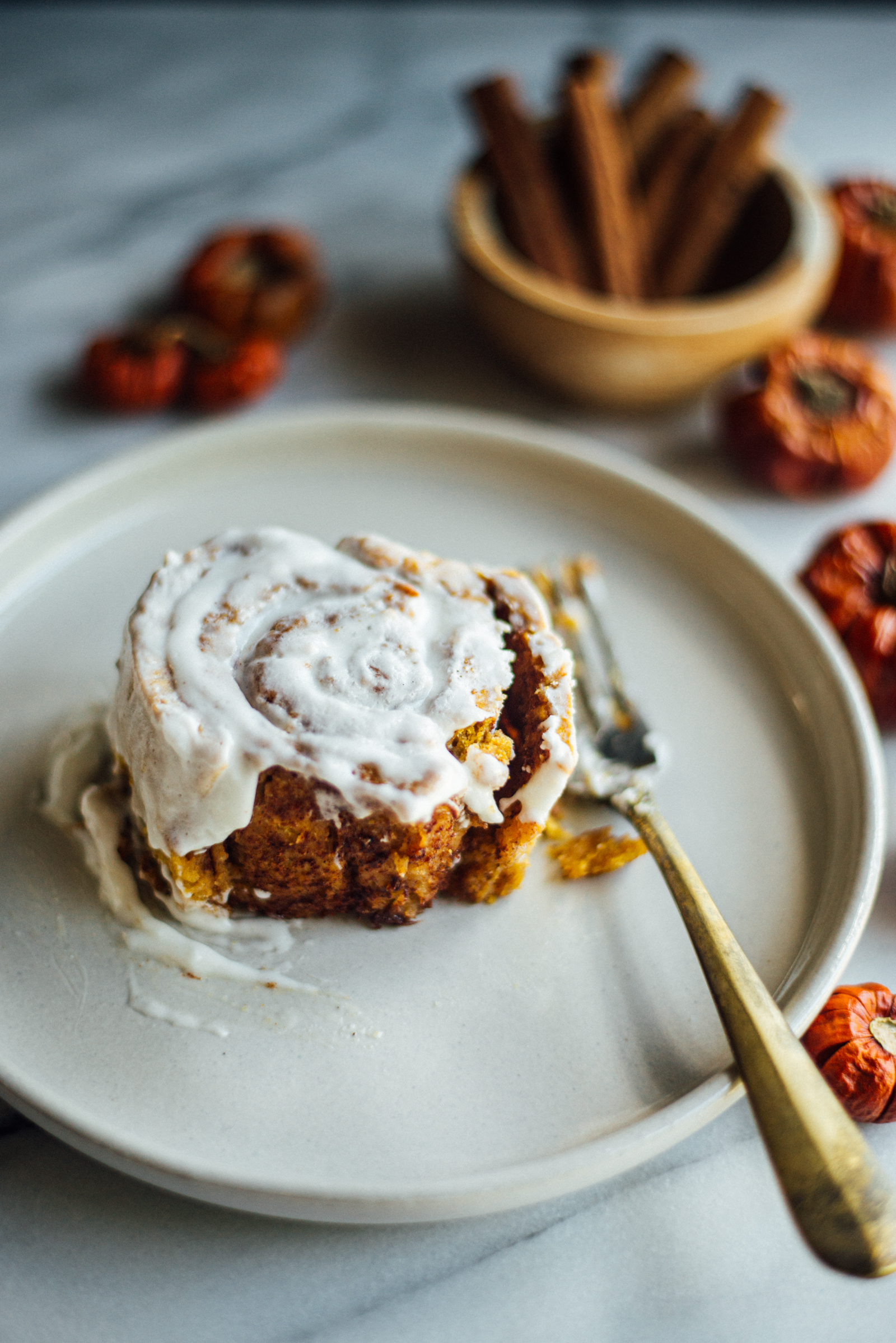 gluten-free pumpkin cinnamon roll on neutral plate with cinnamon sticks and mini pumpkins